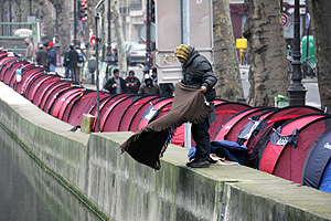 Un 'Sintecho' sacude una manta en el canal al lado de la fila de tiendas. (Foto: AFP)